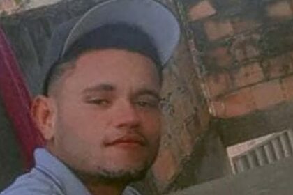 Jovem de boné e camisa branca em uma casa sem reboco