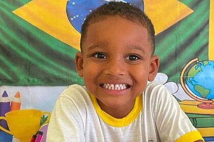 Criança aparece sorrindo e ai fundo a bandeira do Brasil