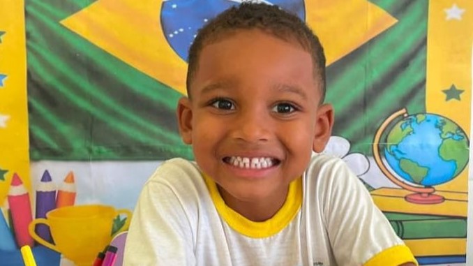 Criança aparece sorrindo e ai fundo a bandeira do Brasil