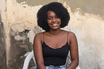 Jovem negra sorrindo sentada em uma cadeira de plástico
