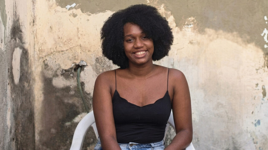 Jovem negra sorrindo sentada em uma cadeira de plástico